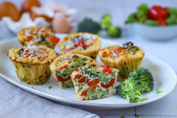 Dozlatova upečené vajíčkové muffiny se zeleninou, bazalkou a čerstvou pažitkou na talíři.