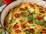 Pečená bramborová frittata s rajčaty a sýrem v červené litinové pánvi.