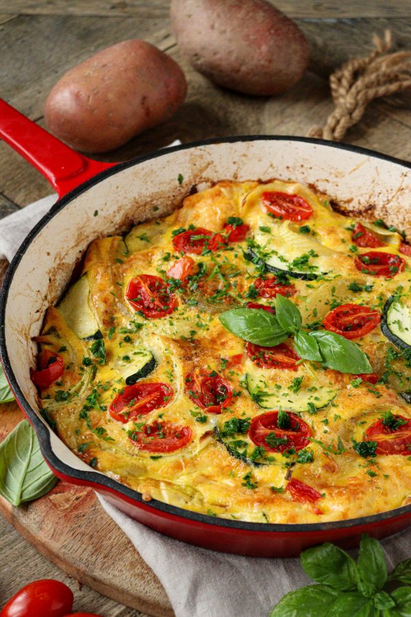 Pečená bramborová frittata s rajčaty a sýrem v červené litinové pánvi.