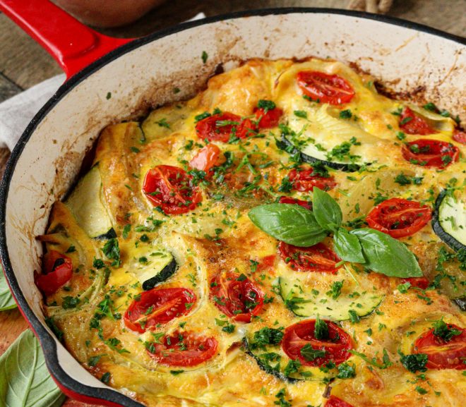Pečená bramborová frittata s rajčaty a sýrem v červené litinové pánvi.