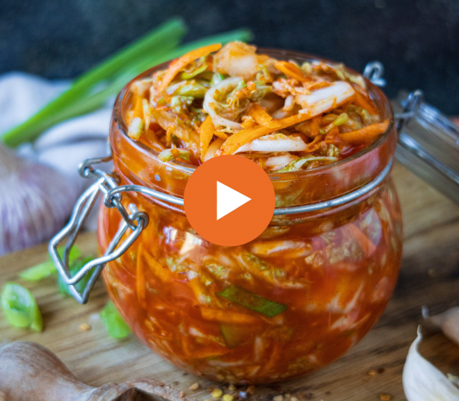 Sklenice s nakládaným červeným kimči z pekingského zelí, jarní cibulky a zázvoru na dřevěném prkénku.