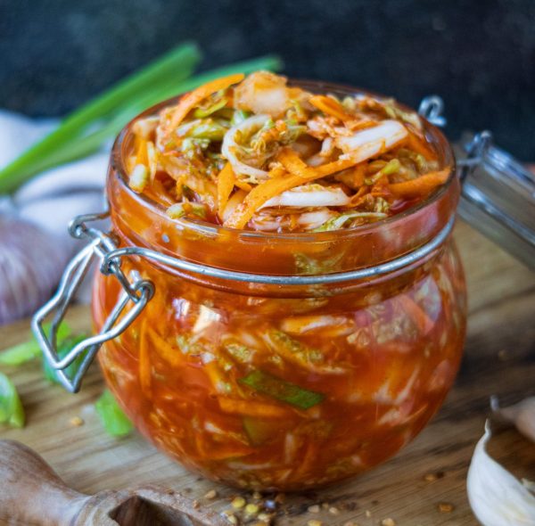 Sklenice s nakládaným červeným kimči z pekingského zelí, jarní cibulky a zázvoru na dřevěném prkénku.
