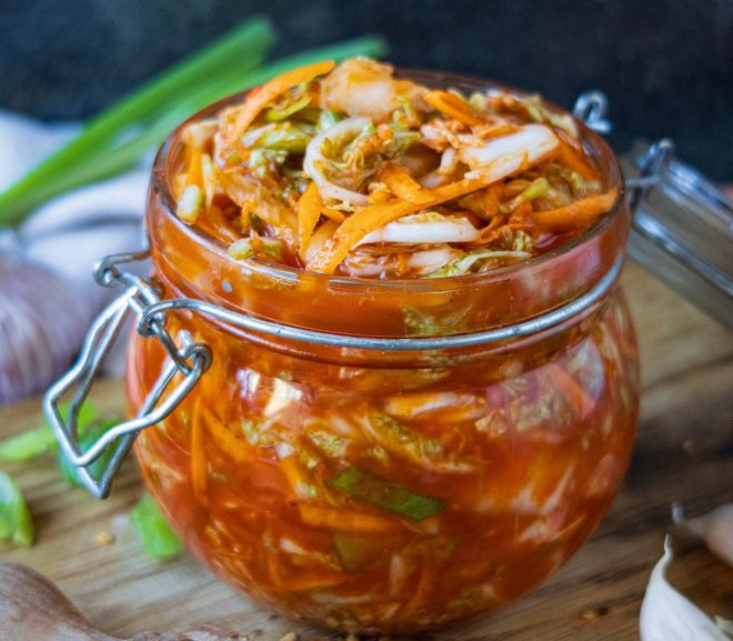 Sklenice s nakládaným červeným kimči z pekingského zelí, jarní cibulky a zázvoru na dřevěném prkénku.